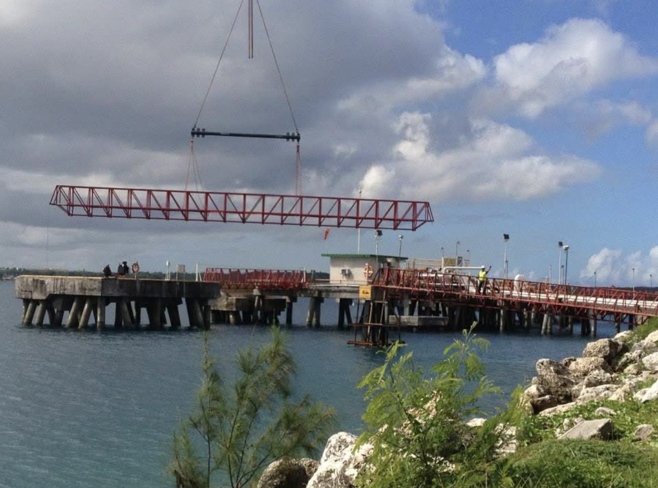 Crane lifting a red steel pipe rack over a fuel pier