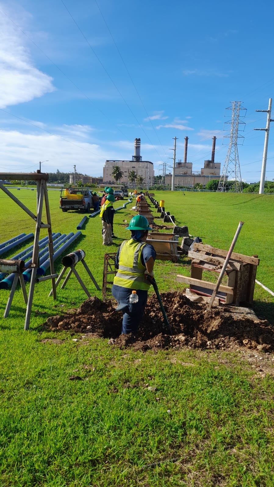 Crew installing a pipeline across a grassy field near a power plant